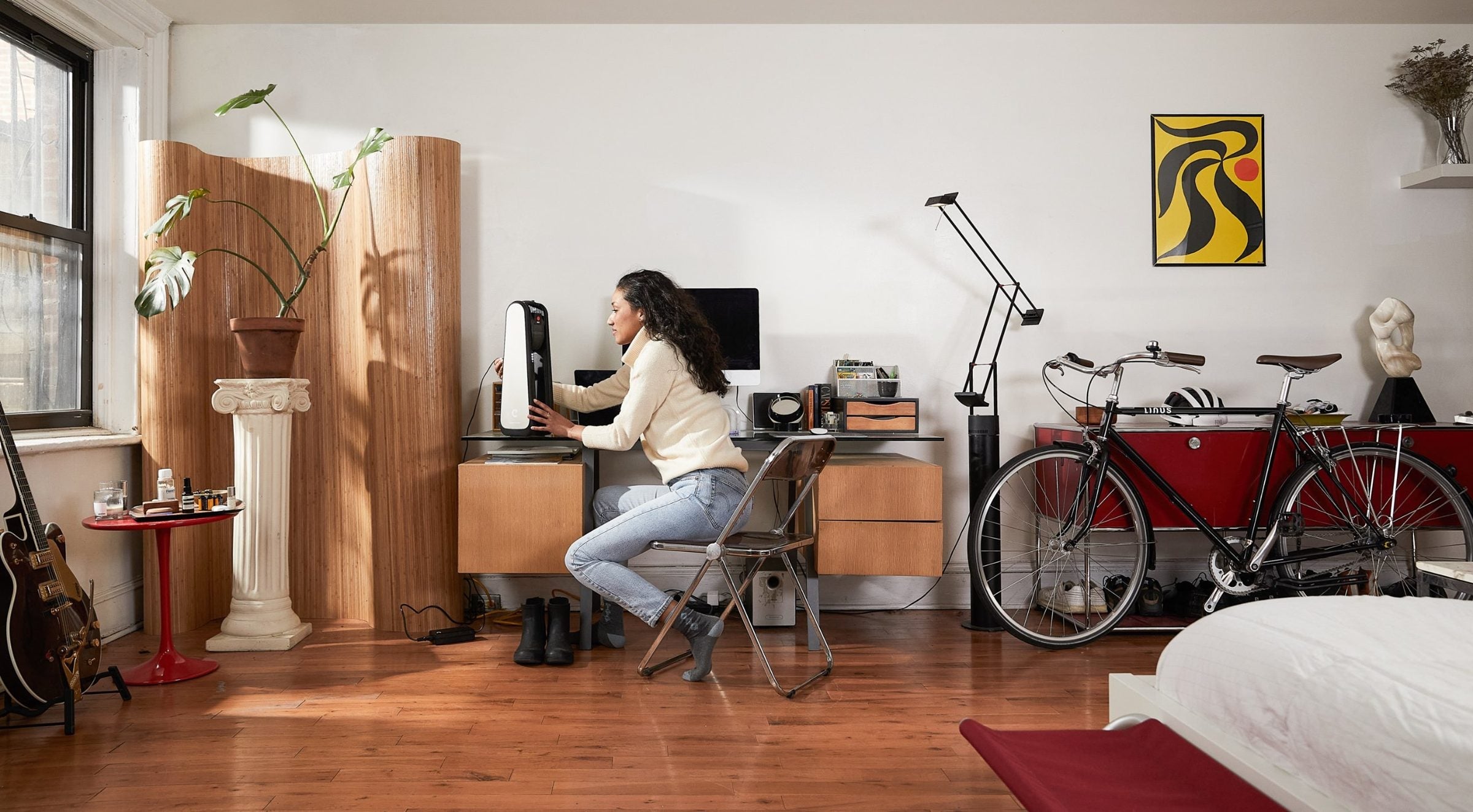 A rider at her desk charging CLIP, her bike parked against the wall
